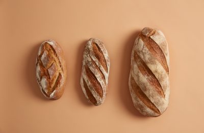 Three tasty loaves of bread arranged on beige background. Gluten free homemade bakery products. Organic freshly baked buckwheat white bread on leaven. Innovative baking concept. Overhead shot
